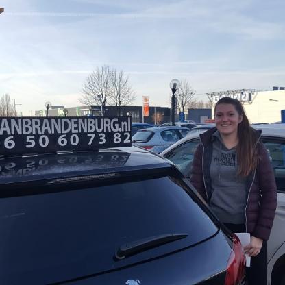Geslaagde leerling met duim omhoog naast de lesauto