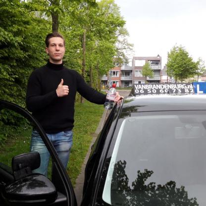 Geslaagde leerling met duim omhoog bij de lesauto