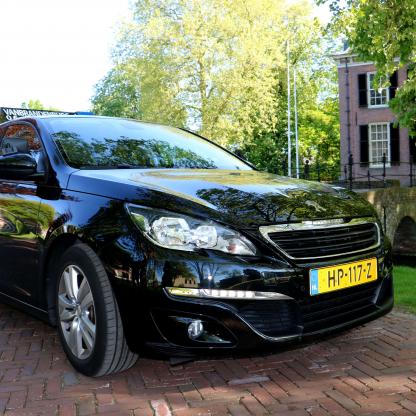 Geslaagde leerling met het rijbewijs naast de lesauto